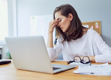 Eine Frau sitzt gestresst vor ihrem Schreibtisch und Laptop