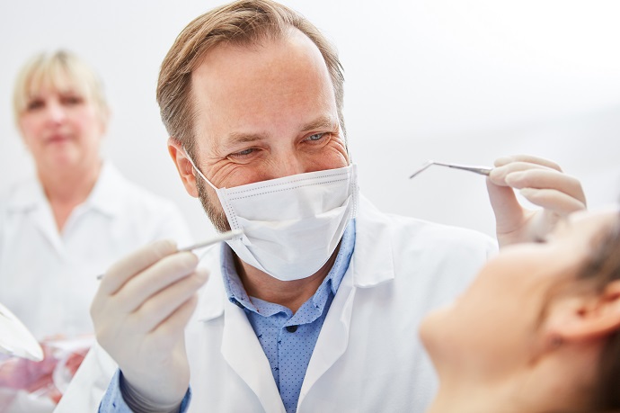 Zahnarzt mit Mundschutz und Handinstrumenten macht eine Untersuchung
