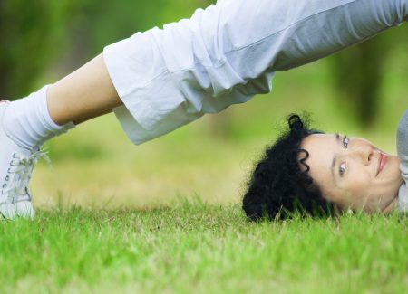 Eine junge Frau macht Jogaübungen auf einer grünen Wiese und schaut in die Kamera