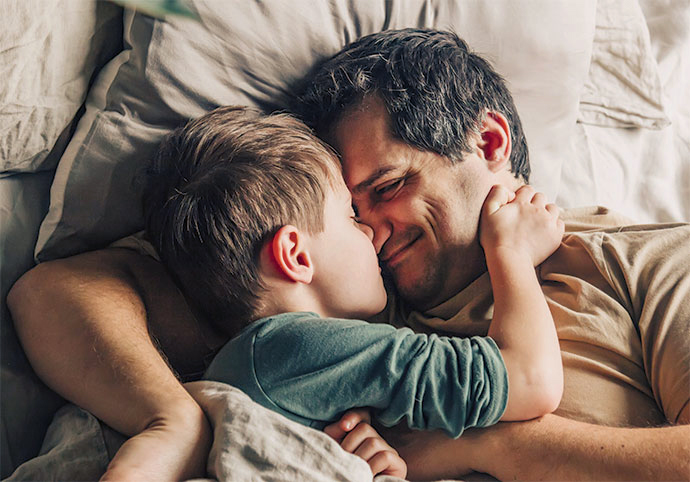 Ein Vater liegt mit seinem Sohn kuschelnd im Bett