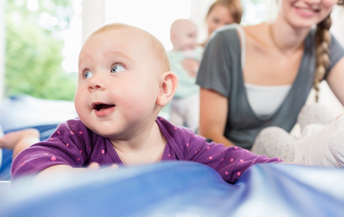 Ein Baby mit der Mutter im Hintergrund liegt auf einer blauen Matte