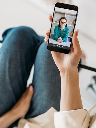 Eine Frau auf dem Sofa spricht per Video-Call auf ihrem Smartphone mit Ihrer Psychotherapeutin