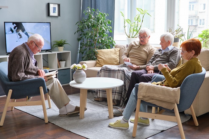 Senioren sitzen in einer Sitzgruppe zusammen, schauen Fernsehen oder lesen