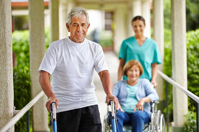 Zufriedene Senioren mit Rollator und Rollstuhl mit einer Plegerin vor einer Rehaeinrichtung