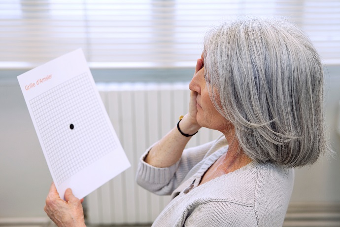 Eine Frau hält sich ein Auge zu. In der anderen Hand hält sie ein Blatt Papier mit einem Amsler-Gitter-Test fest.